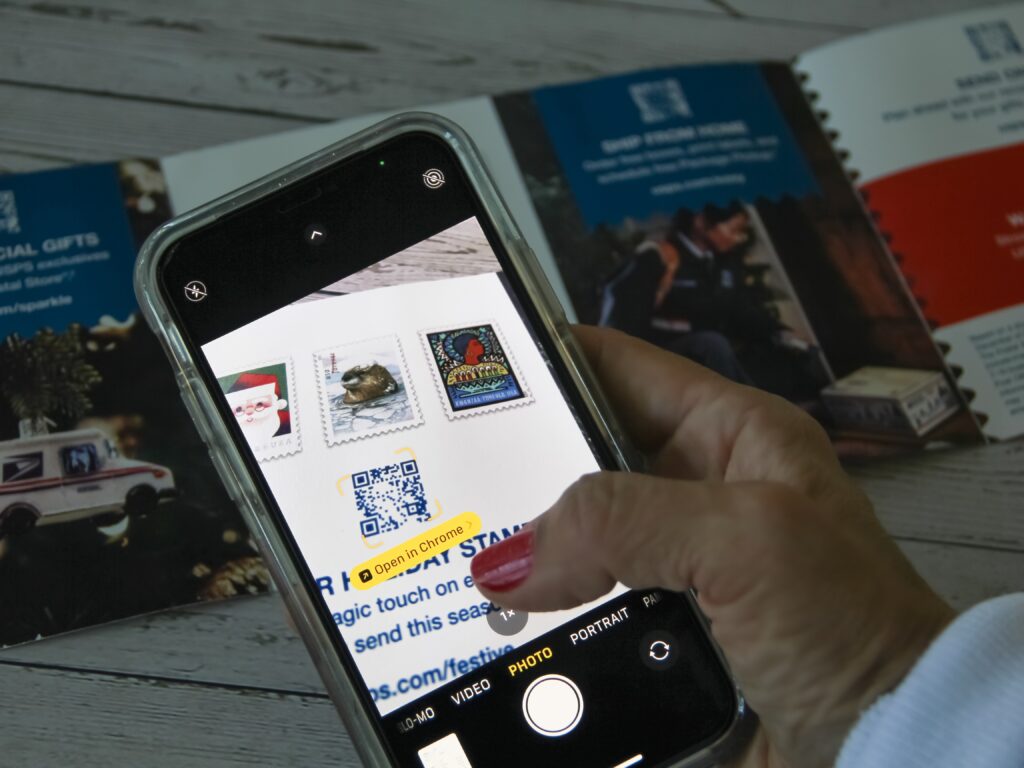Een afbeelding van een vrouw die een telefoon in haar handen heeft waarmee ze een kleine QR code uit een folder probeert te scannen.