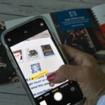 Een afbeelding van een vrouw die een telefoon in haar handen heeft waarmee ze een kleine QR code uit een folder probeert te scannen.