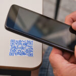 Persoon scant een QR code op een tafel met telefoon.