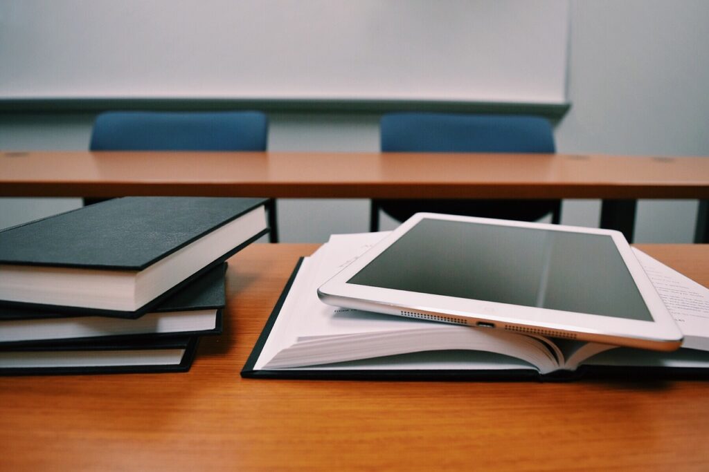 A pile of books and a tablet on a classroom desk.