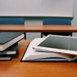 A pile of books and a tablet on a classroom desk.